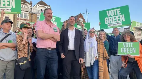 BBC/Cash Murphy A group of people holding placards with 'Vote Green' on them. In the middle are Green Party candidate Rob Yates and party leader Zack Polanski. 