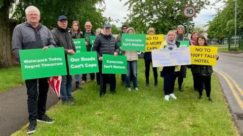 LDRS A number of people with green and yellow signs opposing the water park. 