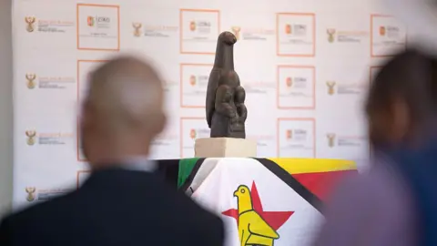 AFP via Getty Images The soapstone sculpture sits on a surface that is covered by a Zimbabwean flag