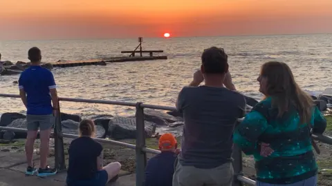 People looking out to sea at the sunrise from Ness Point in Lowestoft