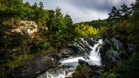 Getty Images A waterfall with ragged rocks, surrounded by trees in Wester Ross in the Scottish Highlands