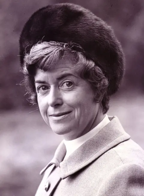 June Spencer in a dark fur hat and plain, lighter coat, in a black and white image