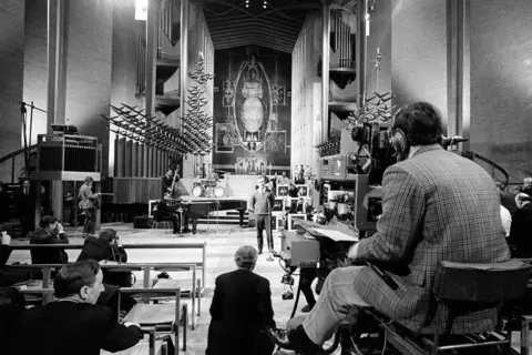 Getty Images A black and white image shows a cameraman sitting in the cathedral filming proceedings. He is wearing headphones and a checked jacket. 