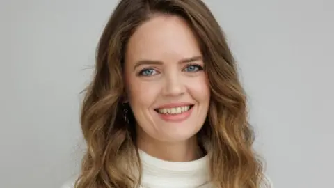 Trása Canavan, with long brown hair, wearing white jumper.