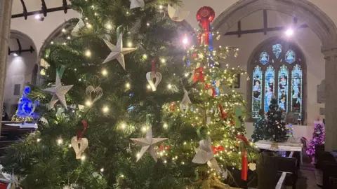 An array of Christmas trees shining with lights inside a church with arched stained windows