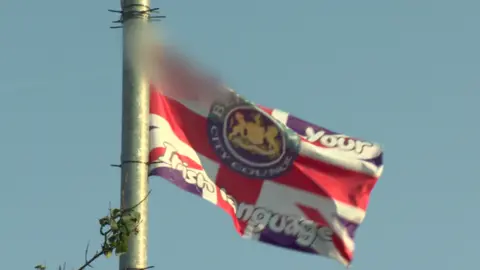 The crest of Belfast City Council and an anti-Irish language message has been printed on a Union Flag. The swear word has been blurred out 