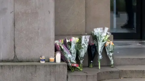 Getty  Flowers and candles at the Australian High Commission in London. There are several bunches of flowers and three candles at the top of stone steps. 