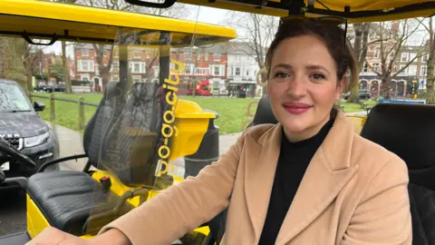 A woman in a beige jacket is sitting in a hire buggy 