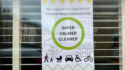 A sign in a window that reads: 'We support the East Bristol Liveable Neighbourhood Trial. Safer, calmer, cleaner'
