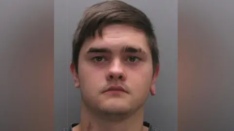 Durham Police Mugshot of Fish. He has dark hair swept across his head and is clean shaven.
