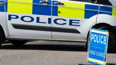 Stock photo of a police car and a police road closed sign