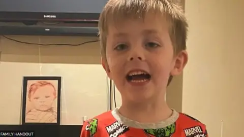 Dylan, with blond hair, looks towards the camera as he is photographed wearing red and grey Marvel-branded pyjamas.
