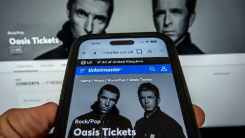 Getty Images A laptop and a smart phone displays the Ticketmaster website with the Oasis gig details on.