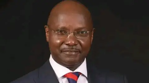 Faith Odhiambo/LSK Mathew Kyalo Mbobu in a dark suit, white shirt and tie