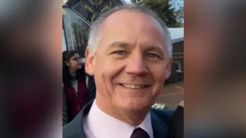 A headshot of Paul Taylor. He is wearing a pink shirt and tie.