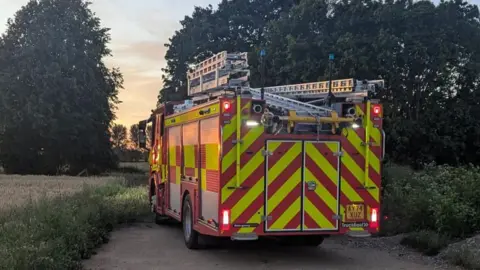 Judith Jacob A red fire engine, parked up in between fields.