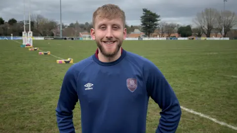 Liam Combellack on a rugby pitch in a blue jumper