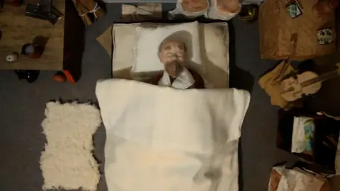 CULTURE VANNIN A still from the film of the puppet tucked up in bed.