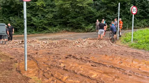 Flooding at Gwaelod-y-Garth, Taff's Well, Cardiff. Road full of mud and stones. Piles of wet mud left behind from the flooding.