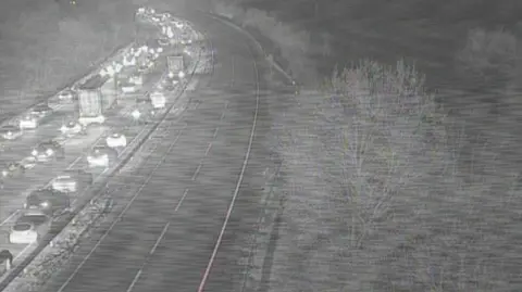 Black and white image of vehicles queuing on the A14. It is dark and the vehicles have their lights on.