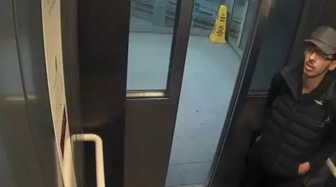 PA Media Salman Abedi, the arena attacker, standing in the corner of a lift wearing a Gillet, cap and glasses.