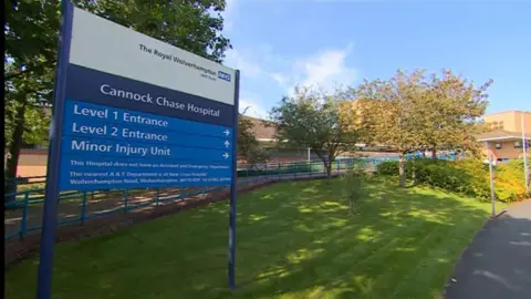 BBC Photograph of the front sign outside Cannock Chase Hospital. The hospital is a yellow-brick building in the background. 