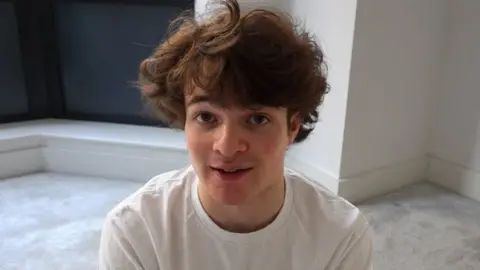 Streamer Tubbo looks directly at the camera. He has thick, short brown hair and wears a white t-shirt