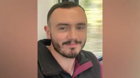 A close up picture of a man who is smiling and has short black hair and a beard. 