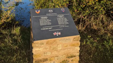 Rockingham Forest Trust Brick-built podium on which stands a slate engraved with the names of the 17 victims of the crash and the three survivors. USA and British flags appear at the bottom of the slate.