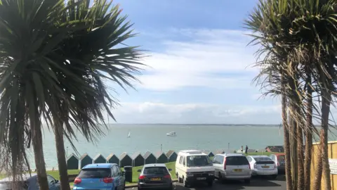 Gurnard Bay, Isle of Wight - beach huts are lined up along the sea front with a play area behind and the sea in front.
