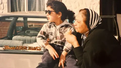 Pavan Bhatt/Leigh Day Old photo showing Pavan as a child, with long dark hair and wearing sunglasses, sitting on a car boot next to his grandmother, who has dark brown hair and is wearing a headscarf