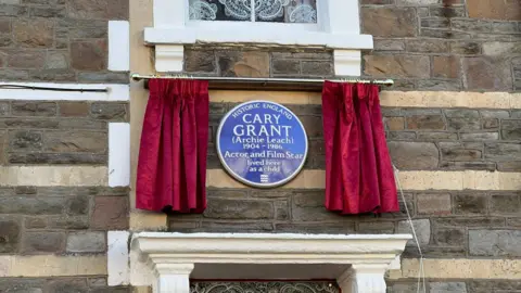 A Historic England blue plaque commemorating Cary Grant behind a red curtain.