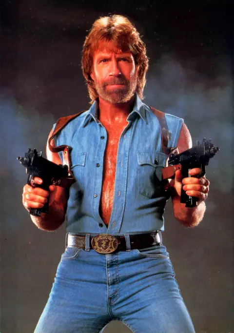 Getty Images Chuck Norris in Invasion USA (1985). He wears a full-denim suit and points two guns