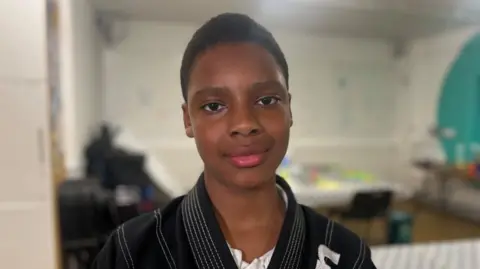 Shiloh is facing the camera, wearing a black martial arts uniform.
