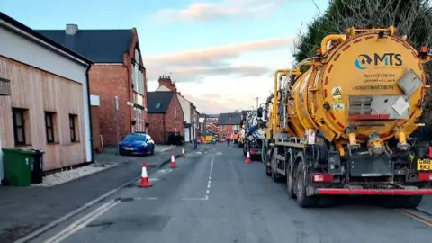 David Adams A narrow residential street which is partly taken up by two tankers, with nearby parking areas coned off