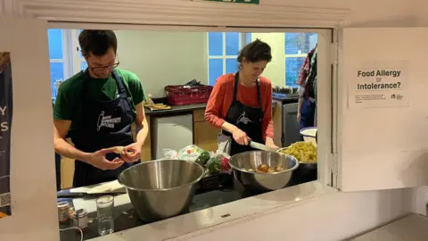 A man and a woman standing at a kitchen counter chopping vegetables including peppers and onions. 