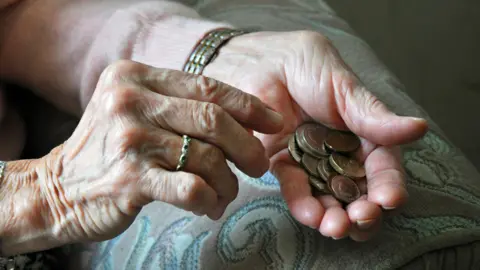 PA Media A close-up of an elderly person's hands with coins in their right hand. They are wearing a watch on their right wrist and a ring on their left hand. 