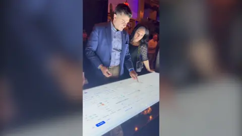 A man and woman placing a bet at a computer screen set in a table.