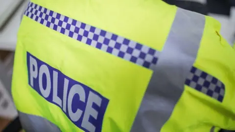 A stock image of a police officer's jacket, which is fluorescent green with silver stripes and a logo which reads police in capital letters.