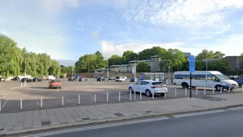 Google A Google Street View of Worcester Street car park, looking on from Worcester Street. The far side is backed by large trees, to the right a brick wall.