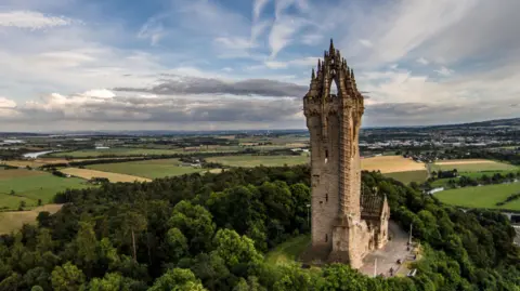 An aerial view of the Wallace Monument at Stirling and a view over trees and fields.