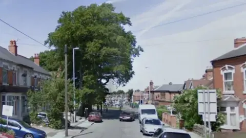 A residential street with trees on both sides of the road and cars along both sides