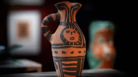 Castle Fine Art Ceramic brick-coloured jug with handle and wide opening. The piece is decorated with a basic black print with stripes, spots and a sun-like face.