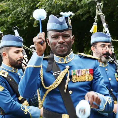 Rosie McGeachan A man in a blue uniform playing a drum in a pipe band championship, with two pipers behind him.