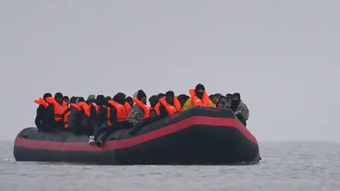 A small inflatable boat is on the water with a number of people wearing inflatable life jackets