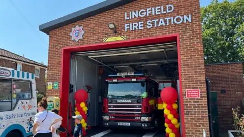 The new Lingfield fire station. A fire engine can be seen in the new entrance, which has 'Lingfield Fire Station' at the top. There are balloons either side of the entrance and an ice cream van outside.