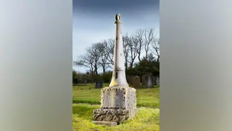 Historic England The monument to James Gall and Grace Darling located in Barrow Cemetery. It is shaped like a 10-foot tall lighthouse and features steps leading to a doorway.