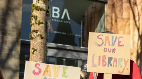 Marion McKinnon With the Birnam library in the background, a banner reading 'Save Our Library' can be seend.