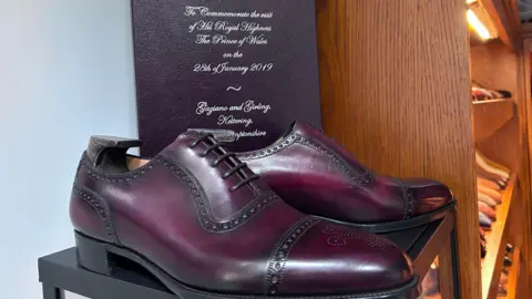 Kate Bradbrook/BBC A pair of shoes made by Gaziano and Girling to commemorate the visit of Prince Charles in 2019. They are on a plinth and are plum in colour with a brogue style detail.