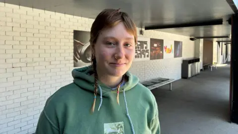 Zac Sherratt/BBC Anna Cruddis, 20, animation student, looks straight at the camera. She has dark blonde hair, with two small plaits, and is wearing a green hoodie